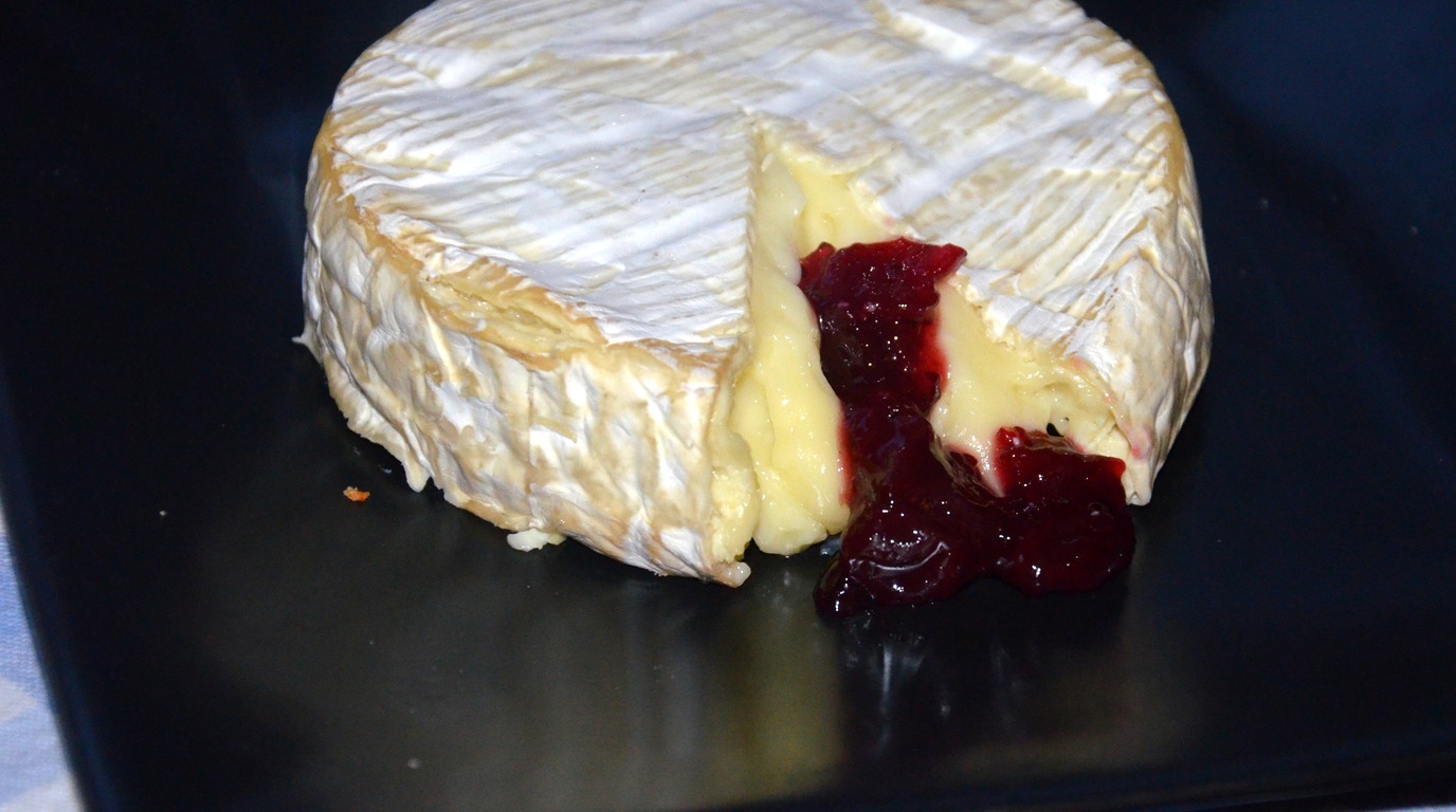 Ultra close-up macro food photograph of cranberry pecan brie pull-apart bread with molten cheese pull and ruby cranberries